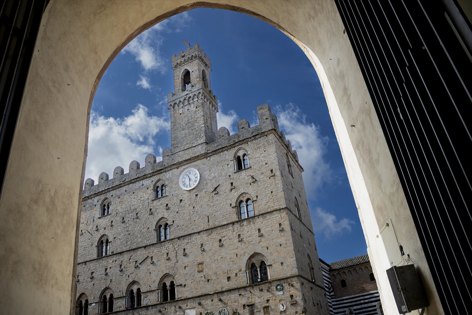 Il Palazzo dei Priori di Volterra inquadrato attraverso un arco medievale
