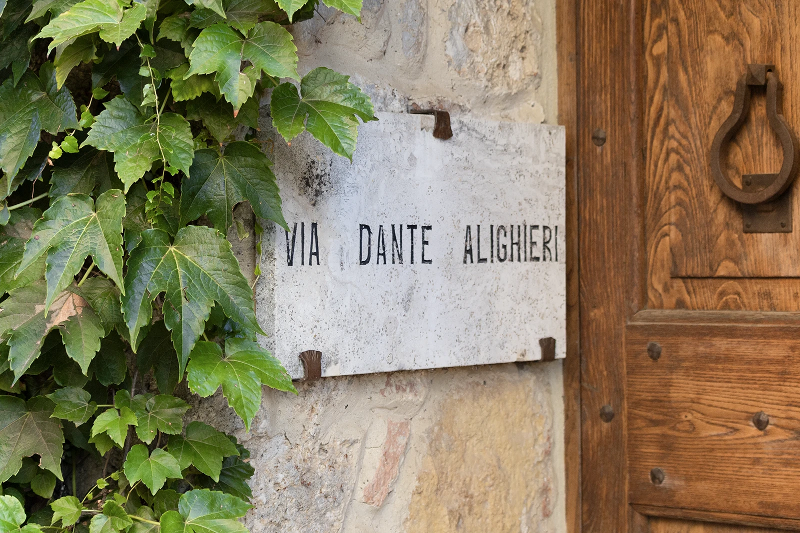 Targa in pietra di Via Dante Alighieri nel centro storico di Volterra con edera e porta in legno