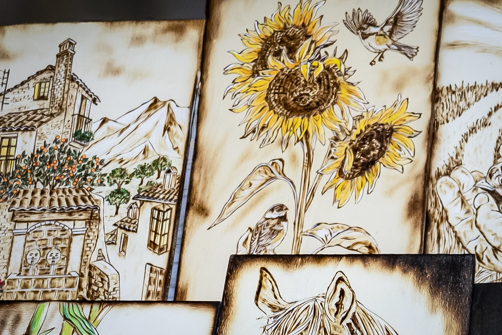 Dettaglio di tavole pirografate: borgo medievale con alberi da frutto, girasoli con uccellini, paesaggio rurale